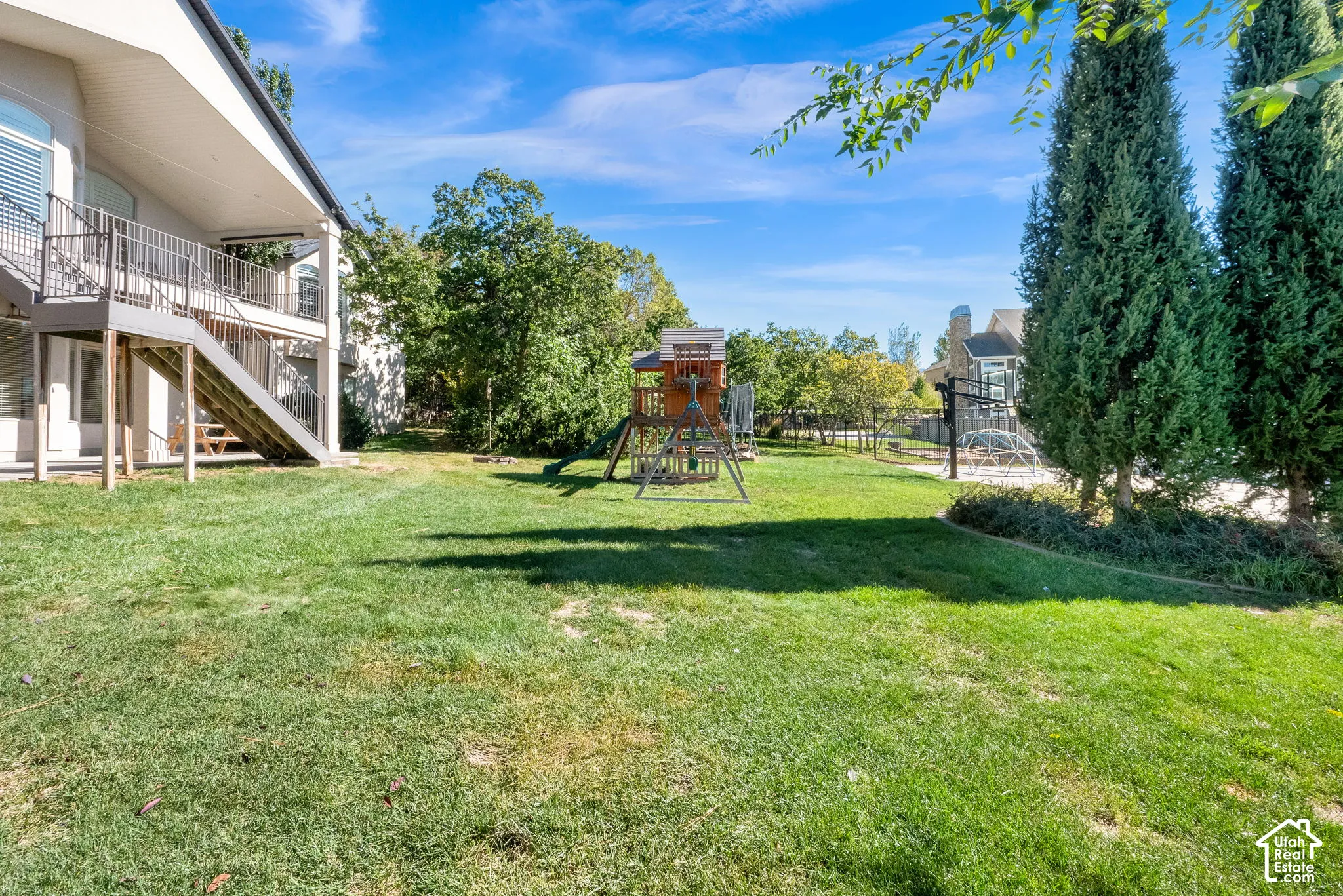 Expansive backyard featuring a tiered wooden deck, metal staircase, mature evergreen trees, and a level grass lawn