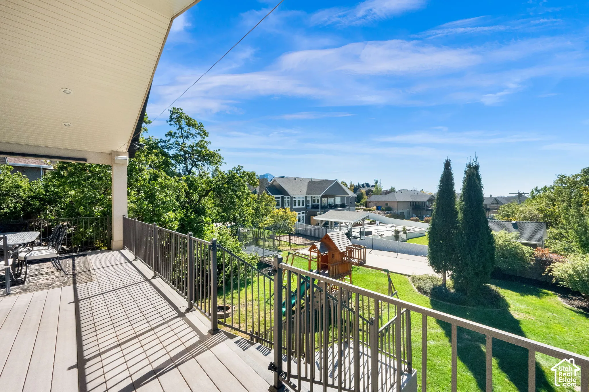 Covered deck featuring composite decking, recessed lighting, and metal railings overlooking a landscaped backyard with mature evergreens