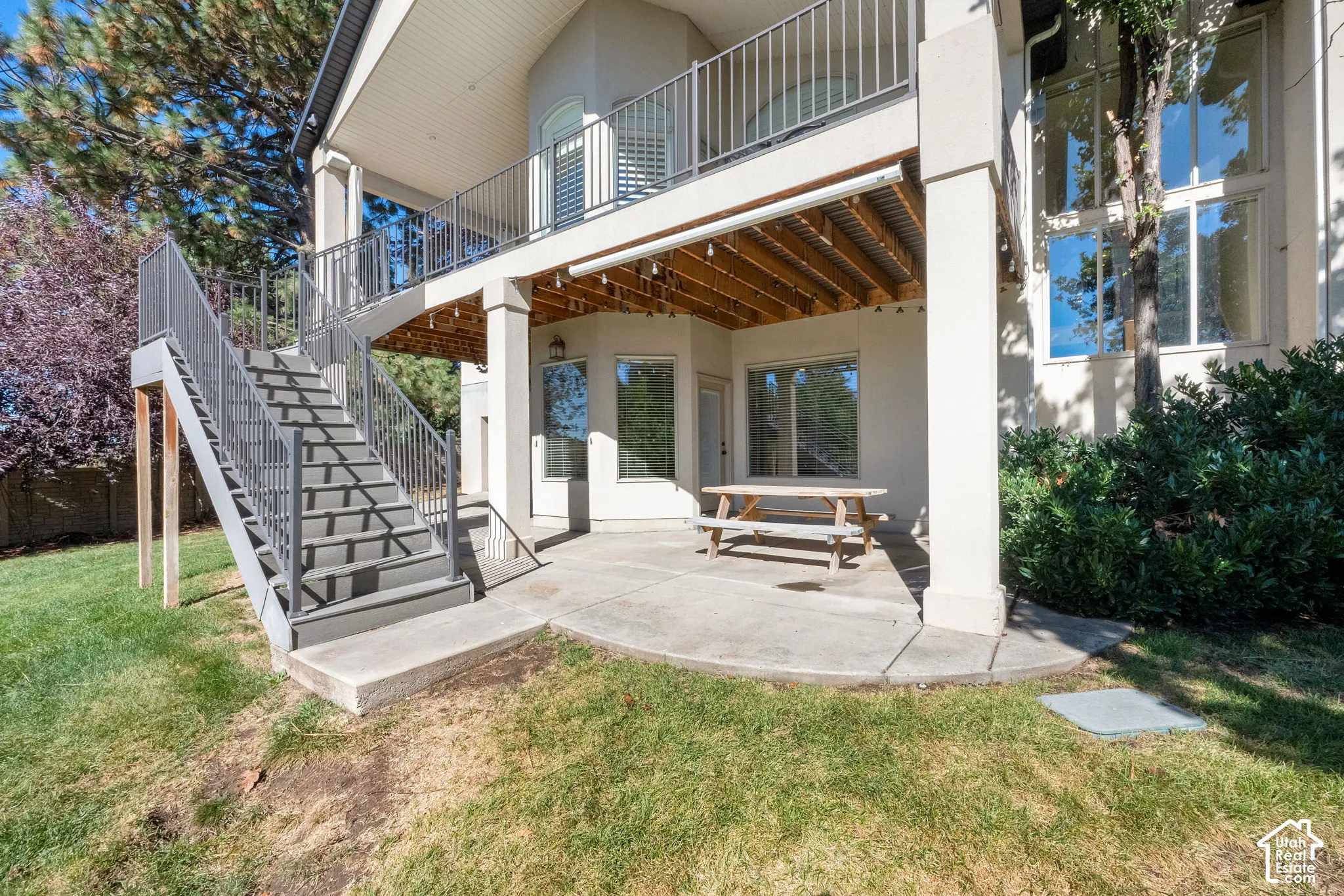 Rear exterior featuring a covered concrete patio, elevated deck with metal railings, and exterior staircase with metal handrails