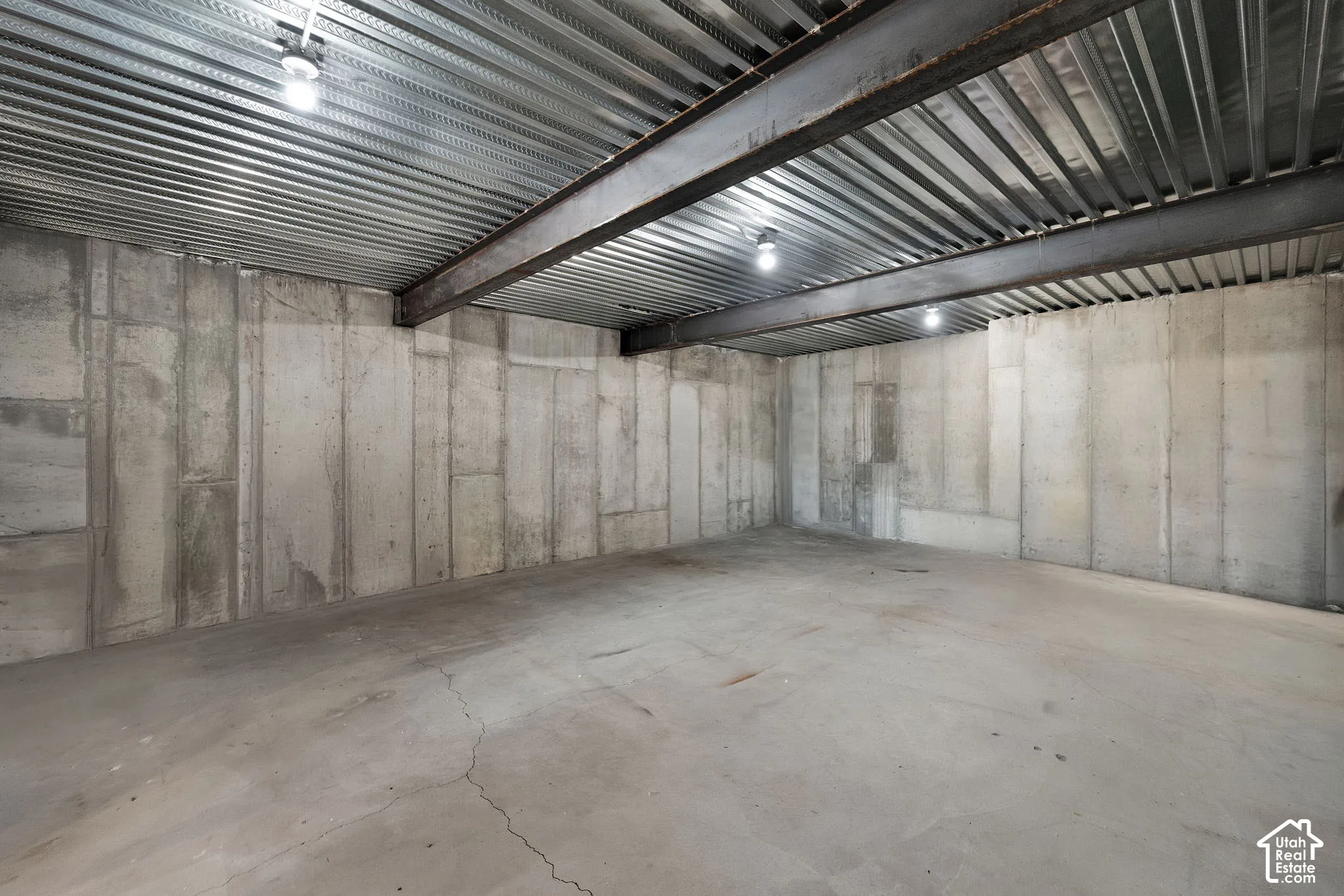 Unfinished space featuring exposed poured concrete walls, structural steel I-beams, corrugated metal ceiling decking, and concrete slab flooring
