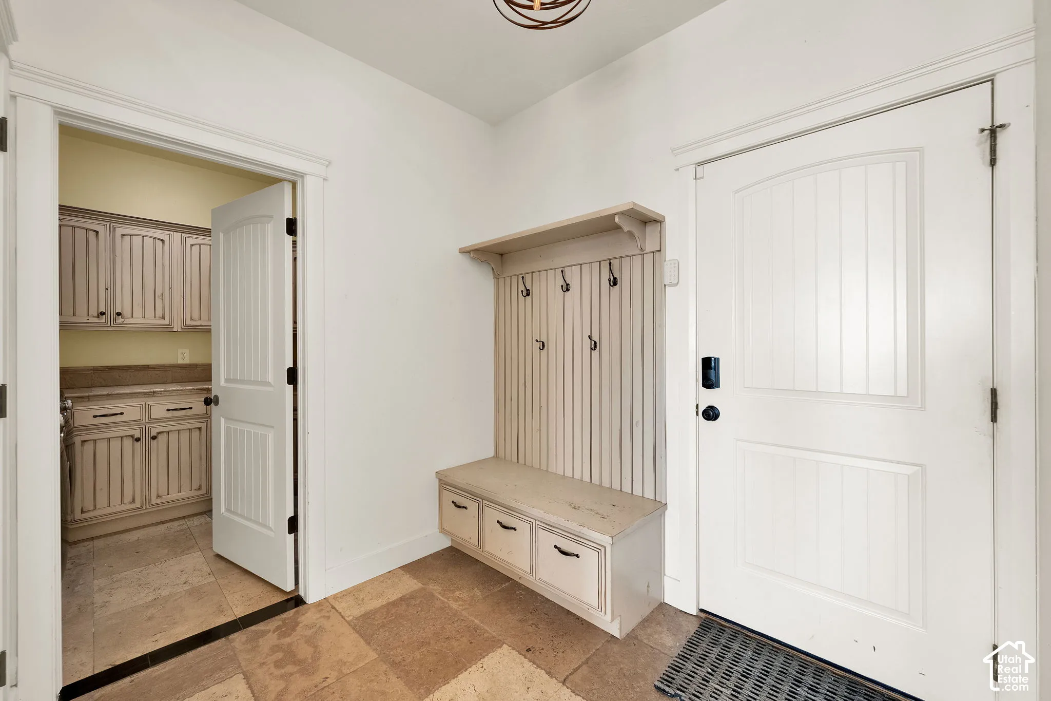 Built-in beadboard mudroom bench featuring integrated cabinetry, upper shelving, and wall-mounted hooks, set against stone-finish floor tiling and a solid-core paneled door
