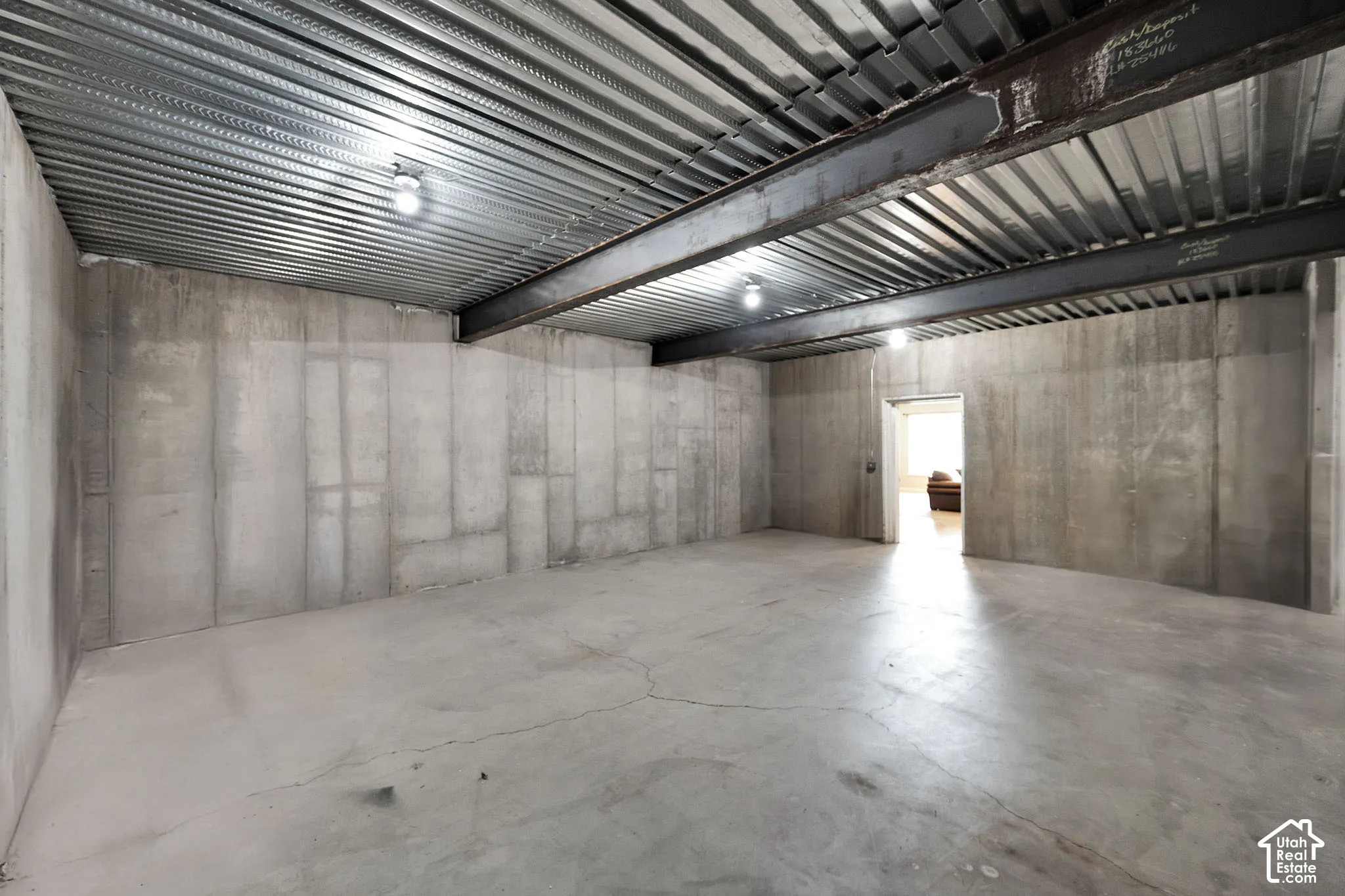 Unfinished interior space featuring poured concrete walls, a exposed steel support beam, and a corrugated metal ceiling deck