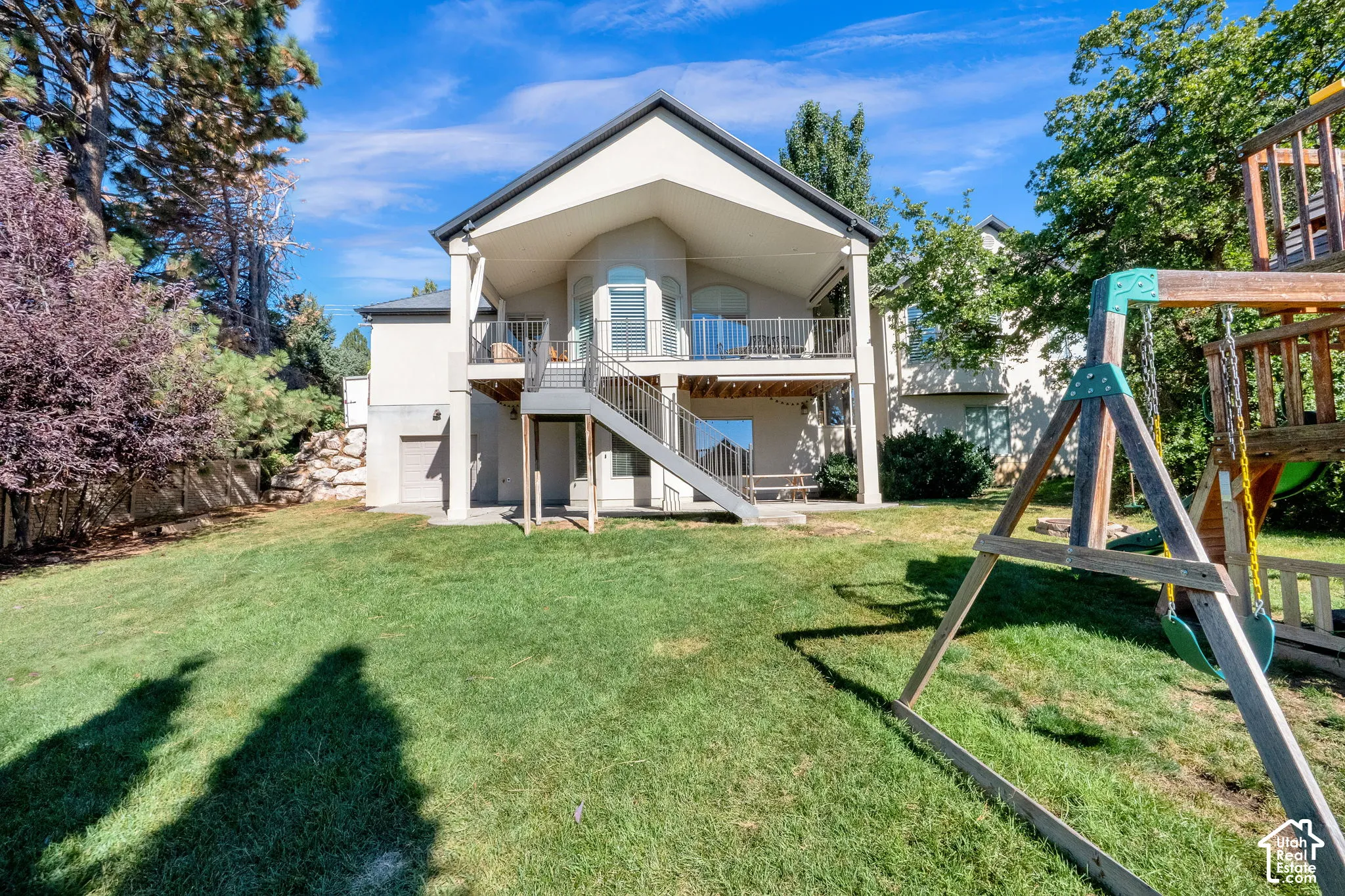 Rear elevation featuring an elevated covered deck, metal railing, exterior staircase, and a concrete patio