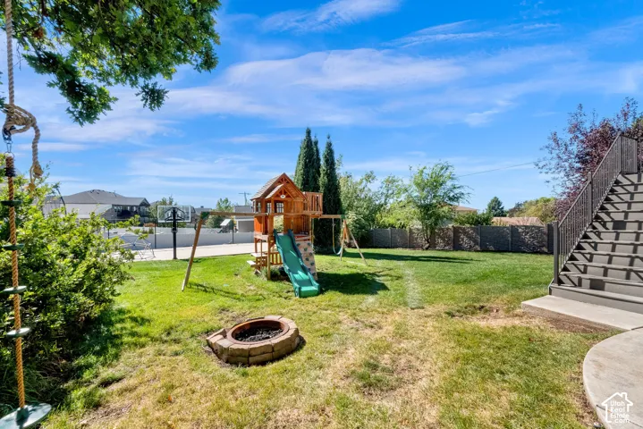 Expansive backyard featuring a stone-lined fire pit, perimeter fencing, and concrete stairs