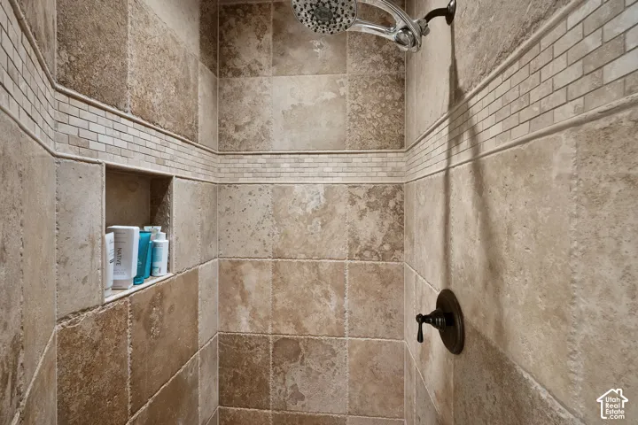 Walk-in shower featuring natural stone wall tile, custom tile inlay accent border, integrated recessed shelving, and a wall-mounted shower head with oil-rubbed bronze fixtures
