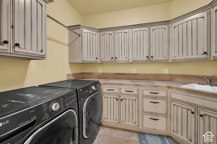 Laundry room featuring custom distressed-finish cabinetry, extensive stone-tile countertops, a deep-basin sink, and tile flooring
