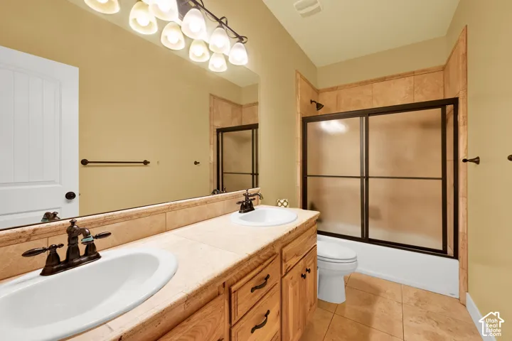 Bathroom featuring dual sinks, stone-tile countertop, wood cabinetry, large vanity mirror, and a tub-shower combination with sliding glass doors