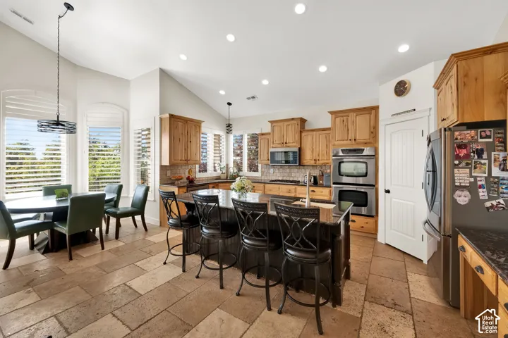 Kitchen featuring natural wood cabinetry, stone-tiled flooring, a dark-toned center island with a stone countertop, built-in double wall ovens, and arched windows with plantation shutters