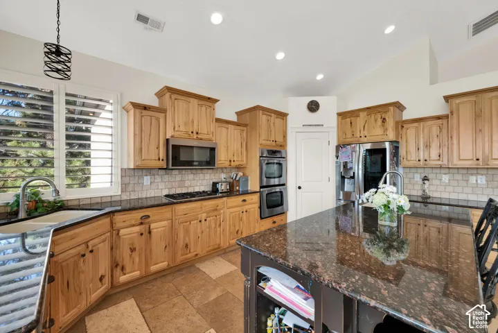 Kitchen featuring natural wood cabinetry, stone countertops, stone tile backsplash, center island with built-in storage, and stainless steel double wall ovens