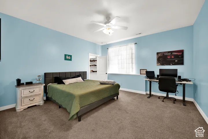 Spacious interior room featuring plush wall-to-wall carpeting, an integrated ceiling fan with light fixture, and a built-in walk-in closet with shelving