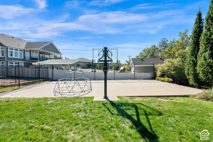 Concrete sport court featuring a basketball hoop, perimeter fencing, and mature landscaping