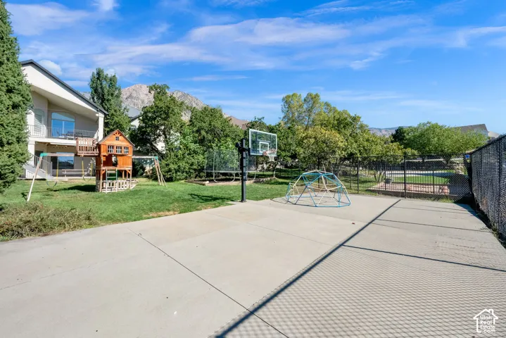 Expansive backyard featuring a concrete sports court, mountain backdrop, mature trees, and perimeter metal fencing