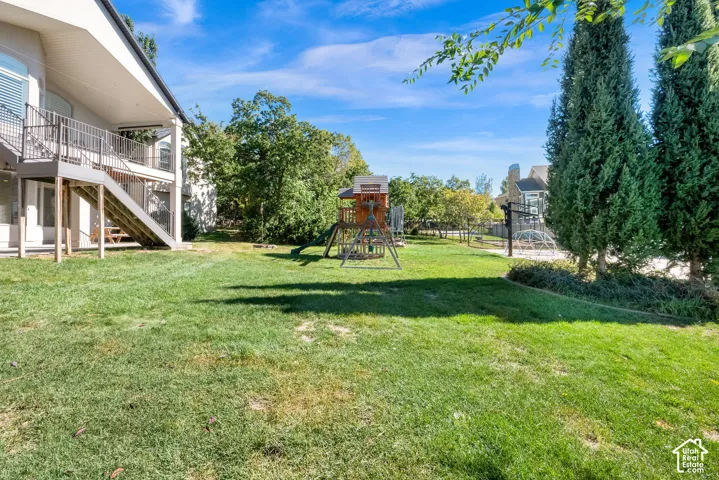 Expansive backyard featuring a tiered wooden deck, metal staircase, mature evergreen trees, and a level grass lawn