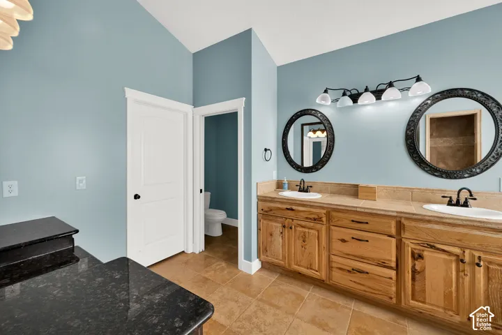 Dual-sink vanity with natural wood cabinetry, stone-style countertop, dual circular mirrors, and multi-light wall fixture
