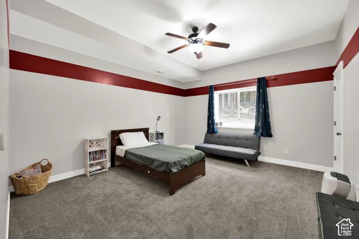 Tray ceiling featuring a central ceiling fan with integrated lighting, window with a sill, and neutral carpeting