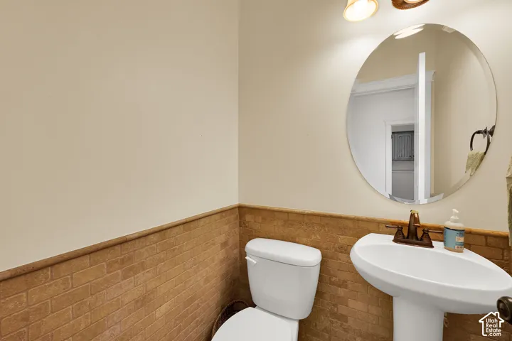 1/2 bath Pedestal sink with oil-rubbed bronze faucet, circular wall-mounted mirror, and half-wall masonry tile wainscoting
