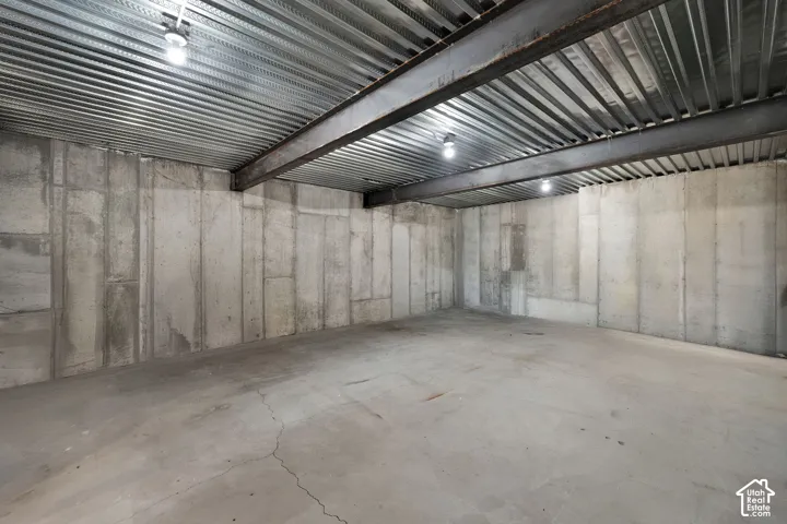 Unfinished space featuring exposed poured concrete walls, structural steel I-beams, corrugated metal ceiling decking, and concrete slab flooring