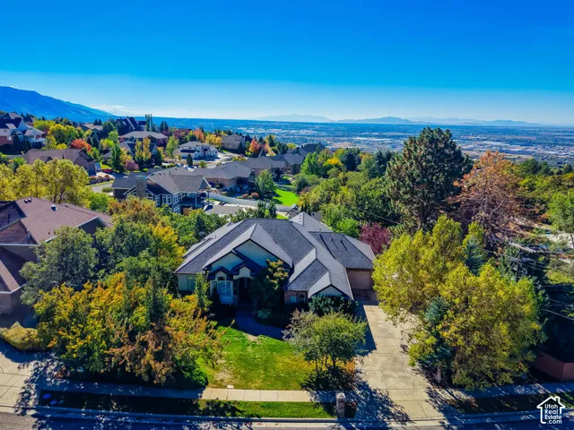 Aerial perspective of a multi-gabled residence featuring a concrete driveway, mature landscaping, and mountain backdrops