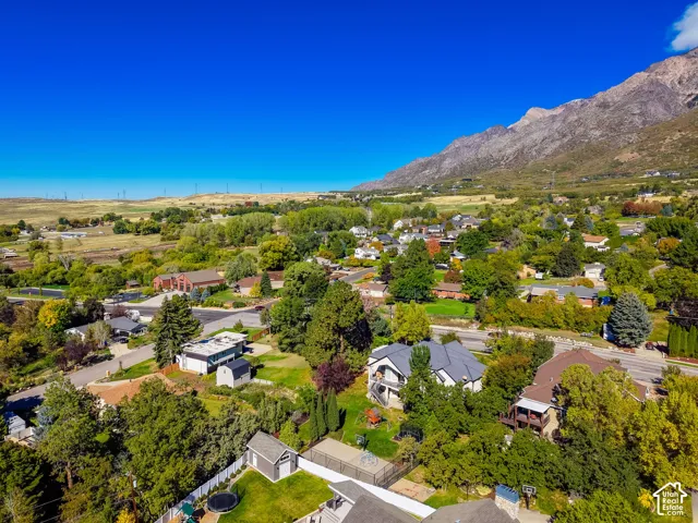 Aerial perspective featuring a multi-level residence, expansive lot with mature trees, fenced backyard, detached storage shed, and a mountain backdrop