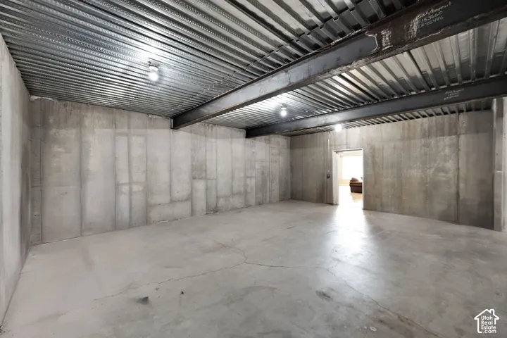 Unfinished interior space featuring poured concrete walls, a exposed steel support beam, and a corrugated metal ceiling deck