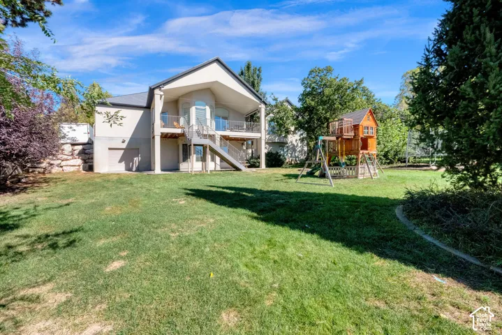 Expansive backyard featuring a manicured lawn, stone retaining wall, raised wooden deck with staircase, and mature trees