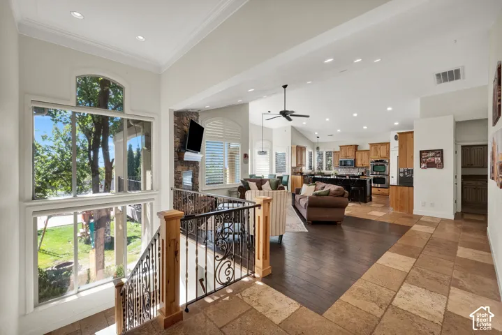 Natural stone tile flooring, wide-plank wood-finish flooring, stone-accented fireplace, decorative metal staircase railing, and recessed ceiling lighting