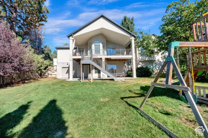 Rear elevation featuring an elevated covered deck, metal railing, exterior staircase, and a concrete patio