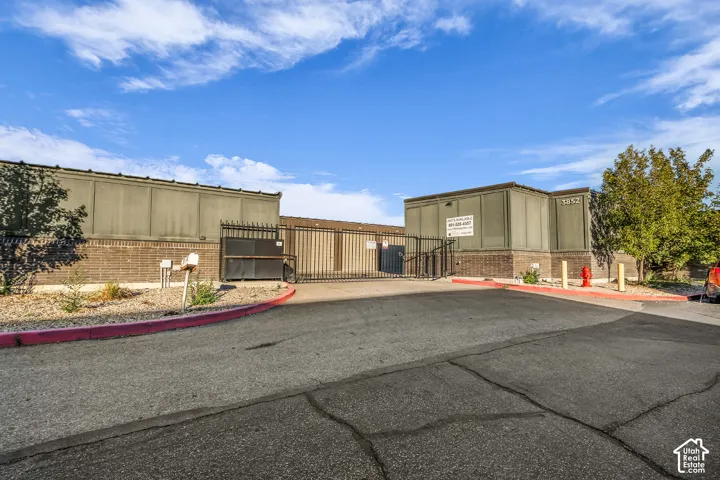 Fenced exterior perimeter featuring brick and panel siding, secured gated entryway, and asphalt surface area