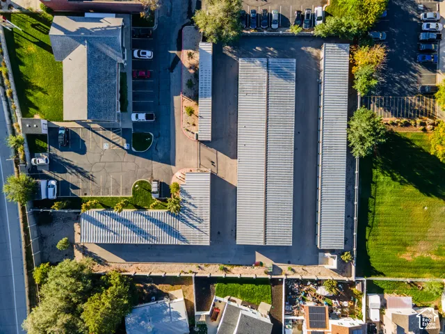 Aerial perspective of a storage facility featuring multiple metal-roofed buildings, paved driveway access, designated surface parking, and perimeter fencing
