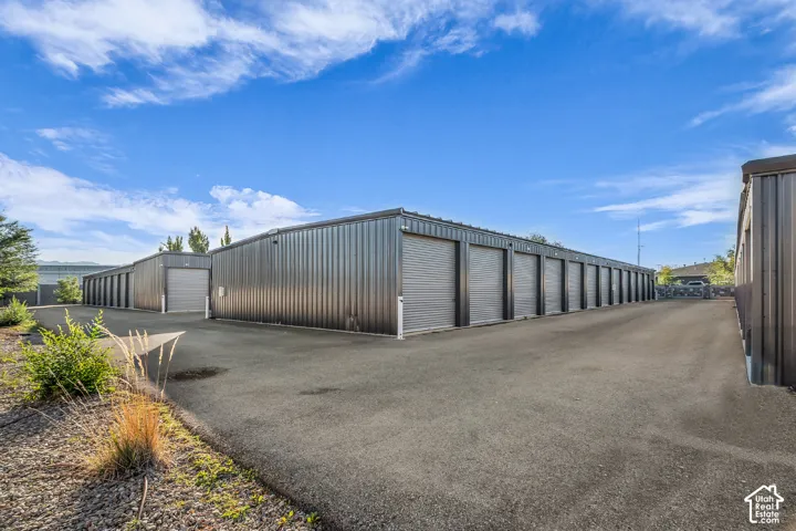 Multi-unit storage facility featuring corrugated metal siding, individual roll-up doors, and paved exterior drive aisles