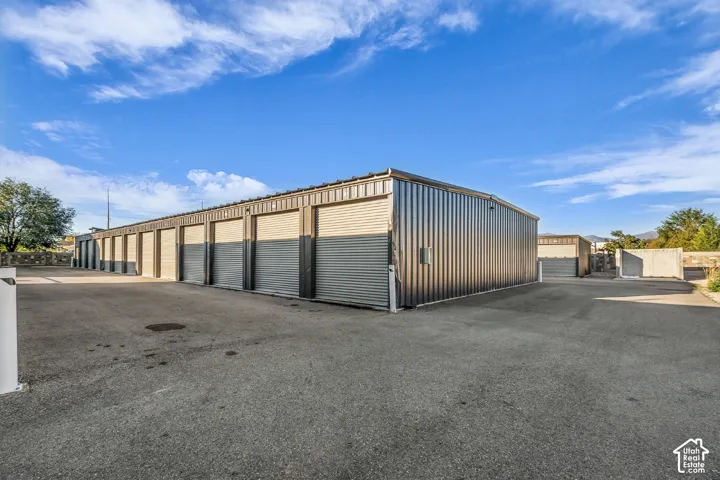 Metal storage facility featuring a series of roll-up doors, metal siding, and expansive asphalt paving