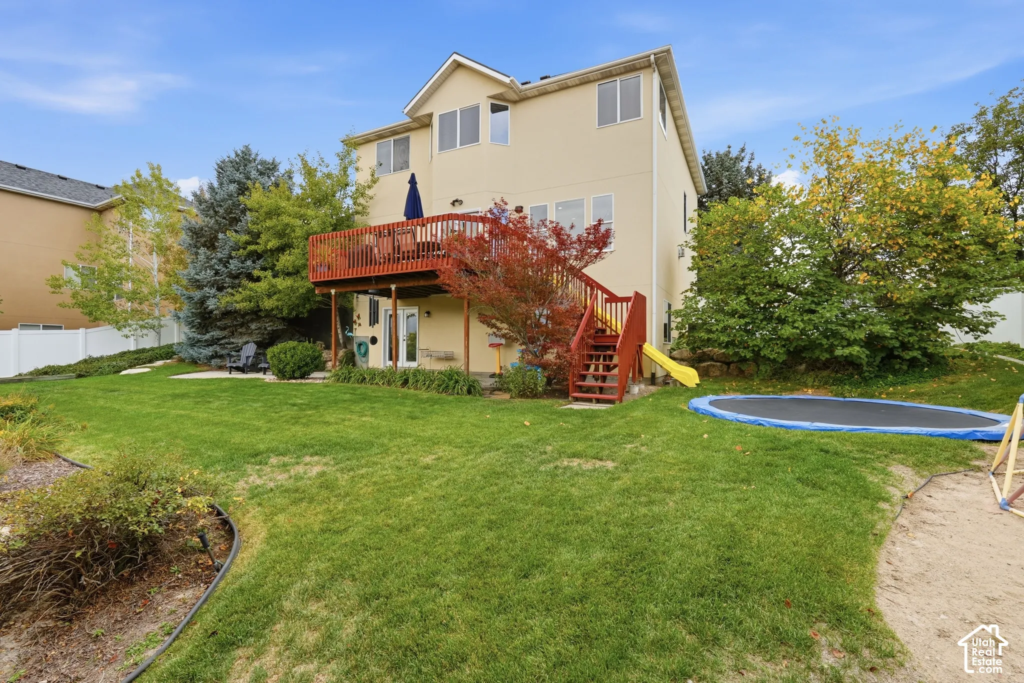 Rear exterior featuring a multi-level wood deck, an exterior staircase with railings, and a landscaped backyard with mature trees
