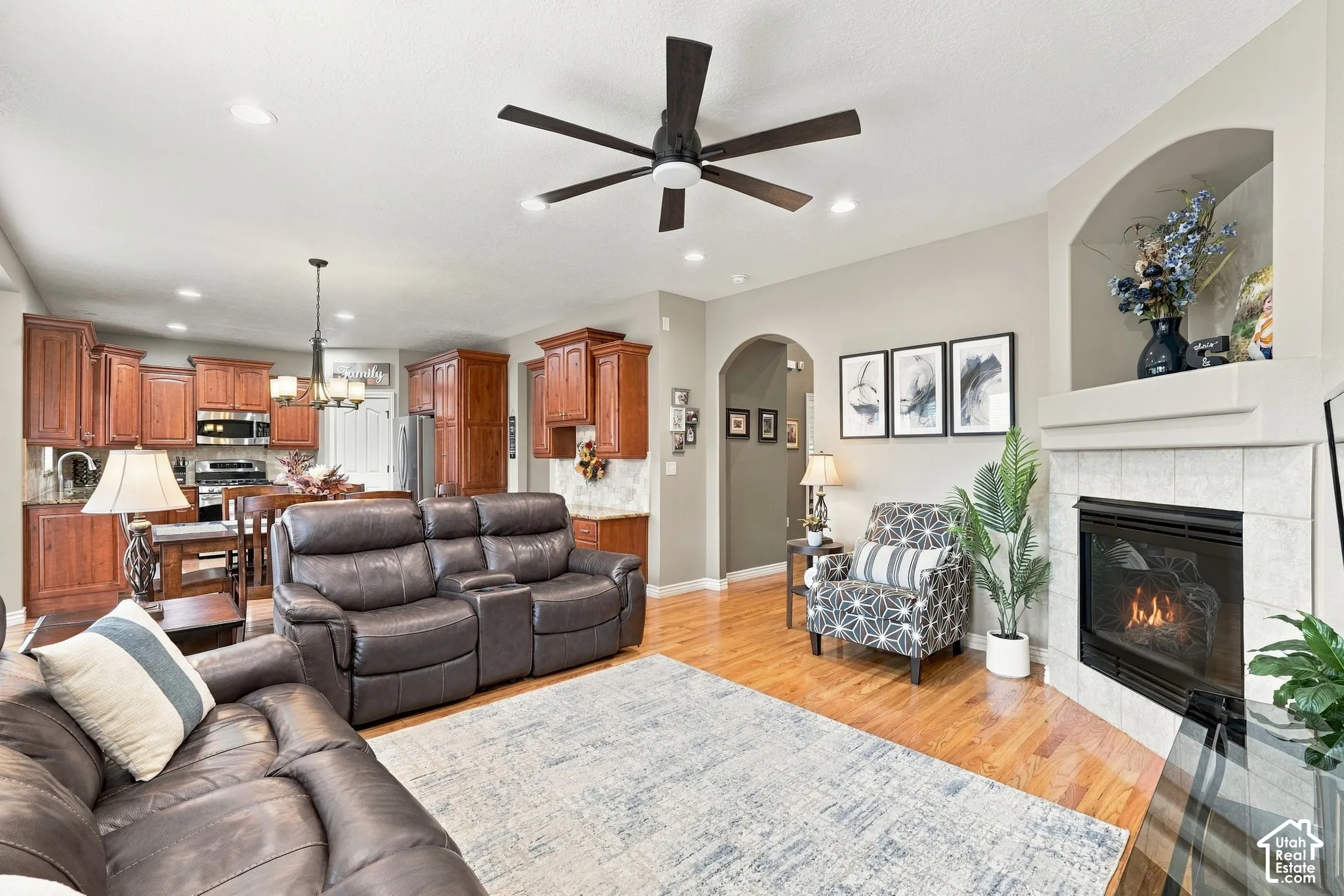 Open-concept interior featuring wood-finish flooring, a tile-surround fireplace with a built-in arched display niche, recessed lighting, and kitchen cabinetry with integrated appliances