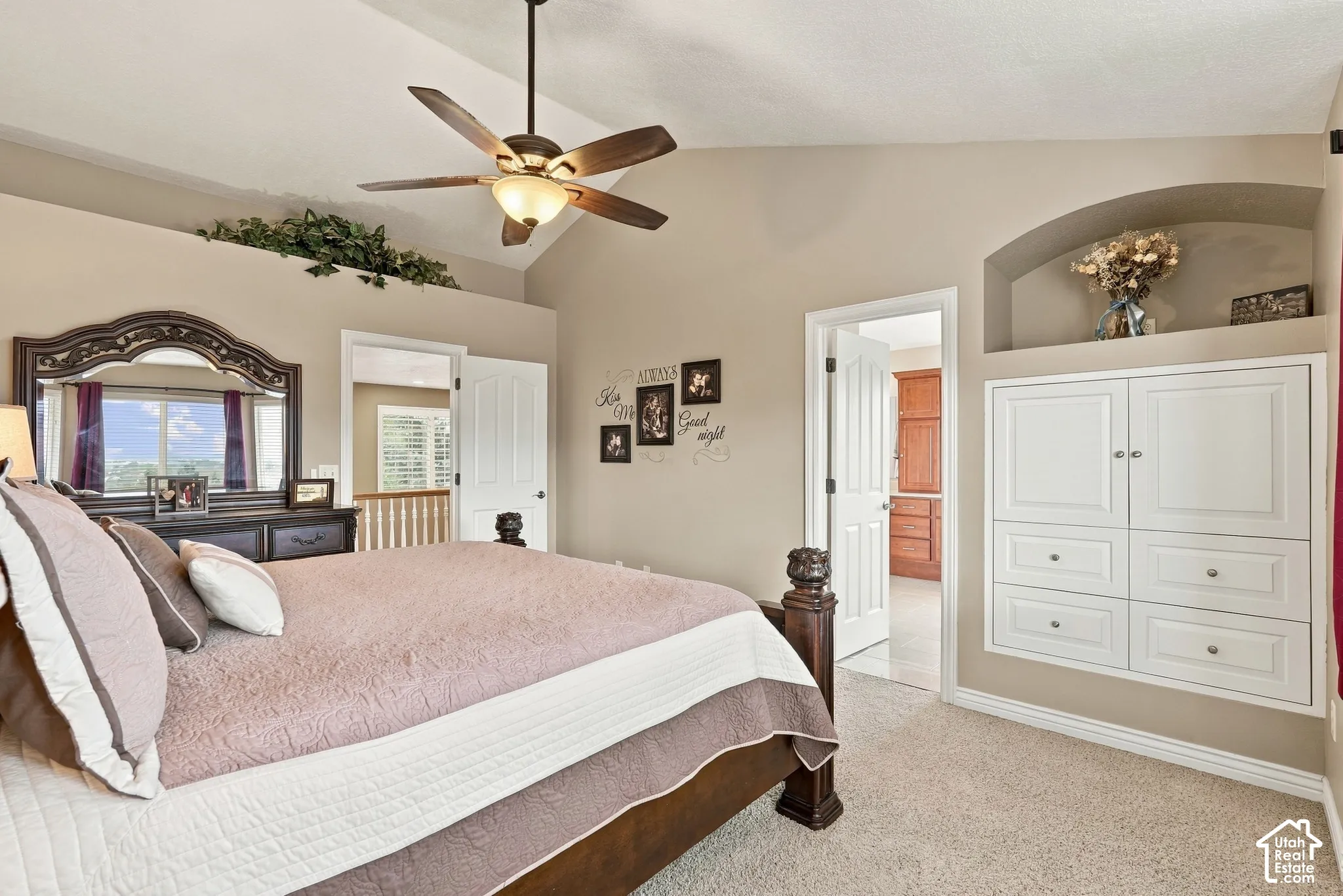 Vaulted ceiling with a centrally mounted ceiling fan and light fixture, complemented by built-in wall cabinetry featuring an integrated recessed arched display niche