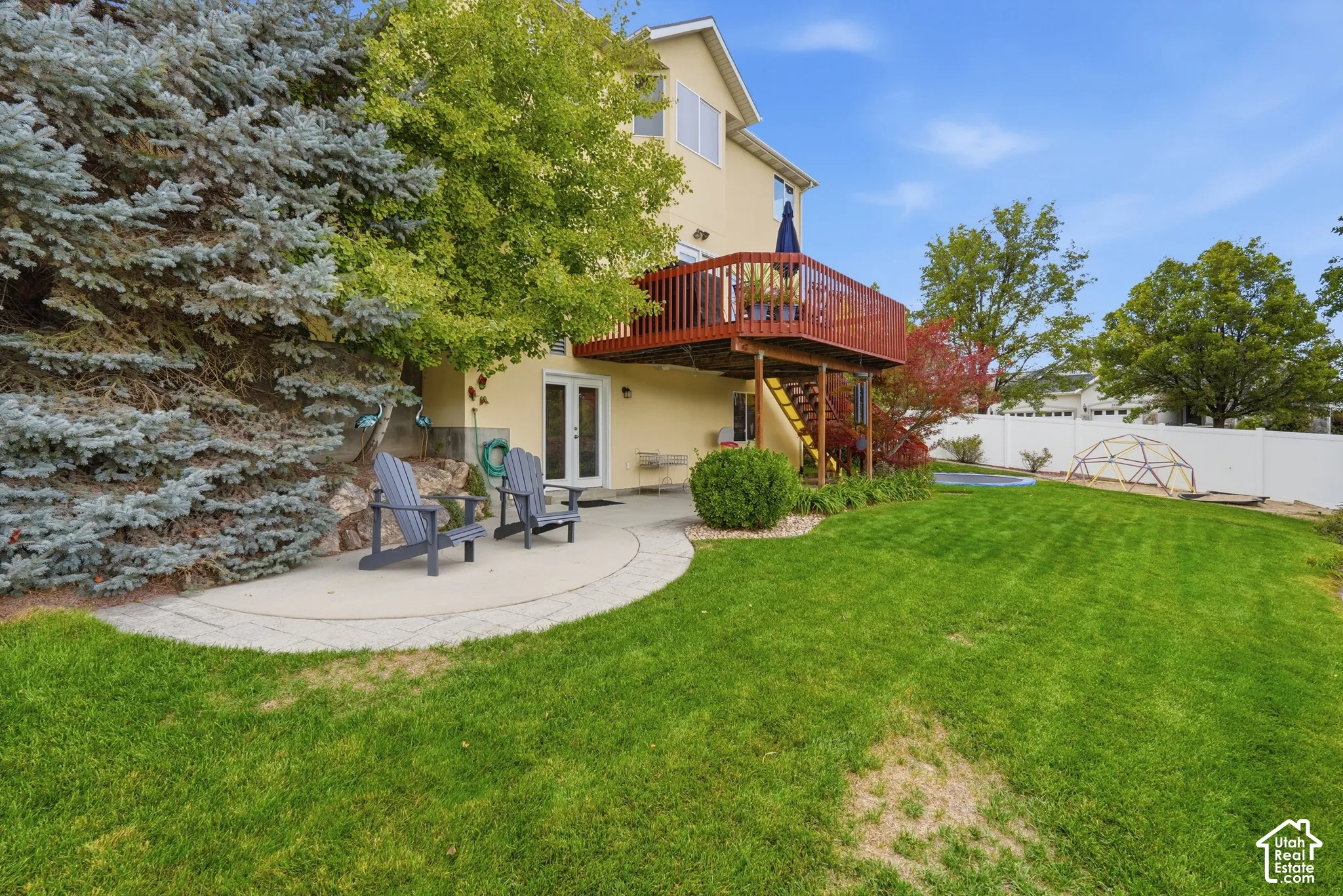 Multi-level exterior featuring a raised wooden deck with a staircase, a concrete ground-level patio, natural stone retaining wall, and a fenced backyard