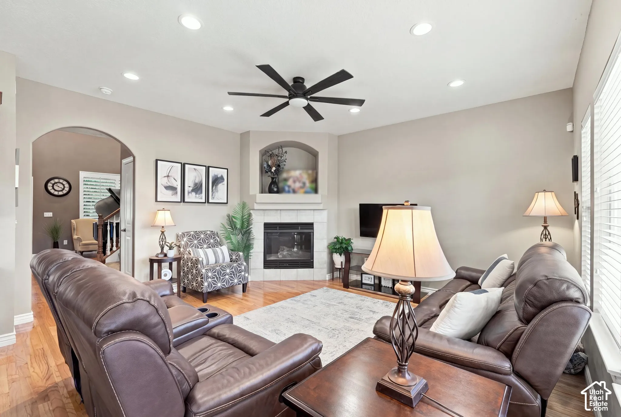 Living area featuring wood-finish flooring, recessed lighting, ceiling fan, corner fireplace with tile surround, and arched entryway
