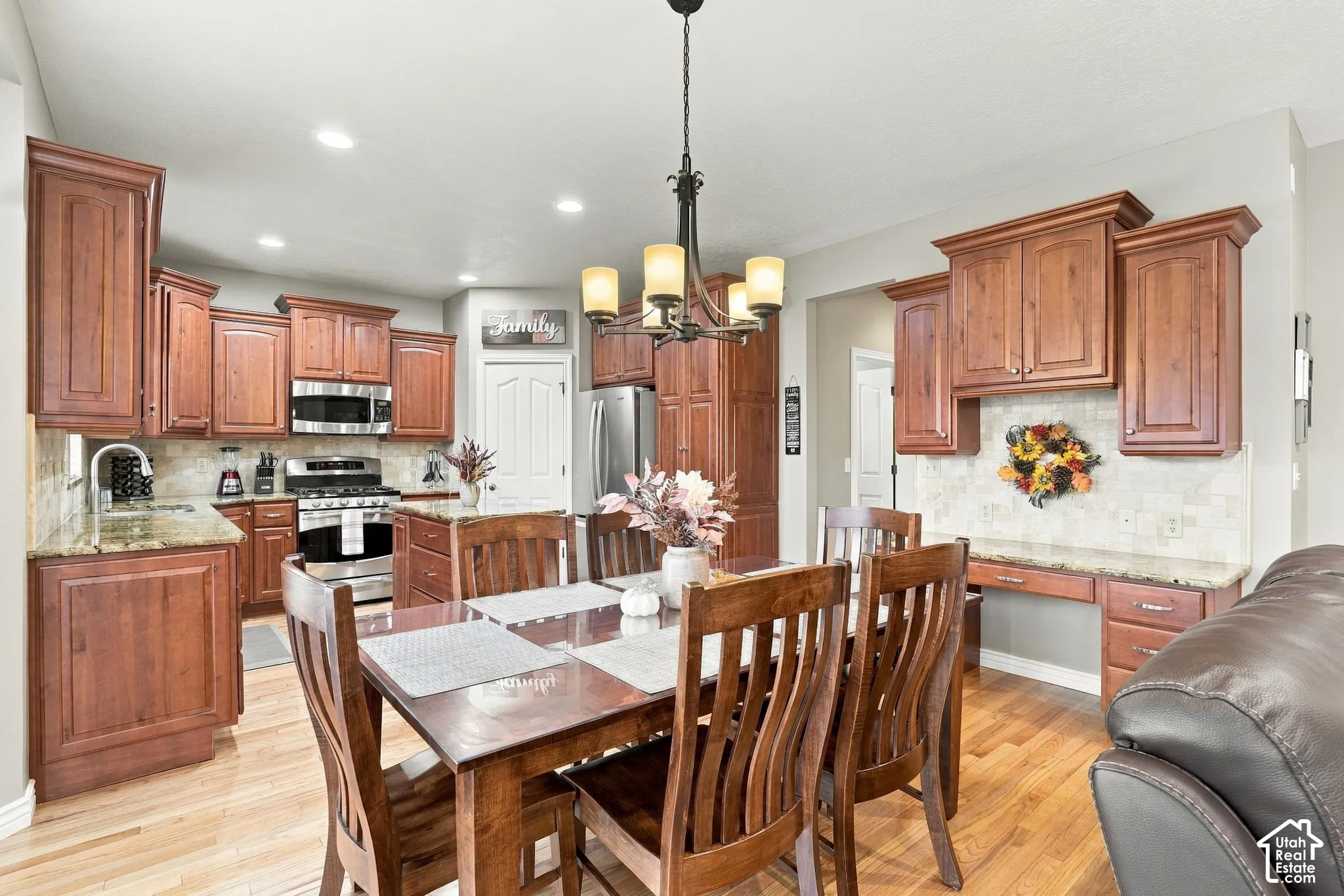 Kitchen featuring stained wood cabinetry, stone-surface countertops, stone tile backsplash, wood-finish flooring, and a multi-light chandelier