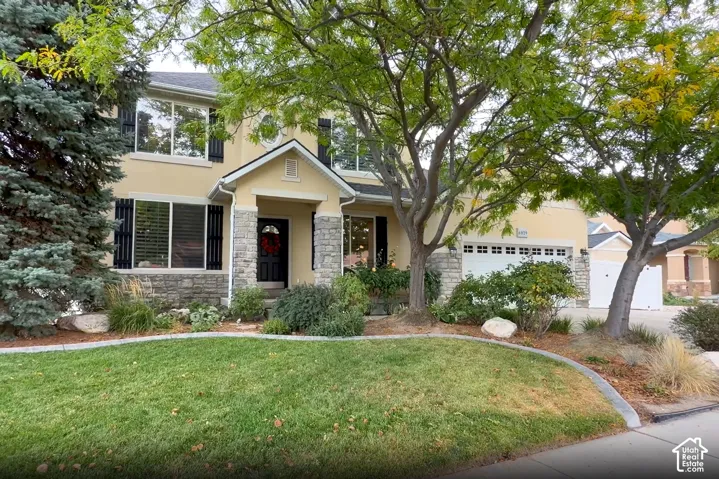 Two-story exterior featuring stucco siding, stone veneer accents, dark louvered shutters, a covered entryway, and a multi-car garage