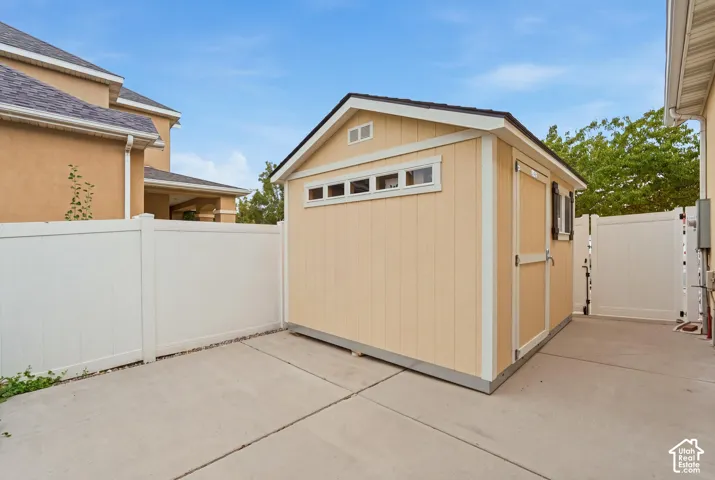 Detached storage structure featuring horizontal trim, a transom window, and a concrete foundation, enclosed by white vinyl privacy fencing