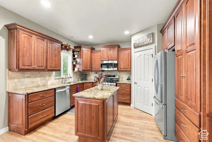 Kitchen featuring wood cabinetry, stone-finish countertops, stone tile backsplash, wood-finish flooring, and stainless steel appliances
