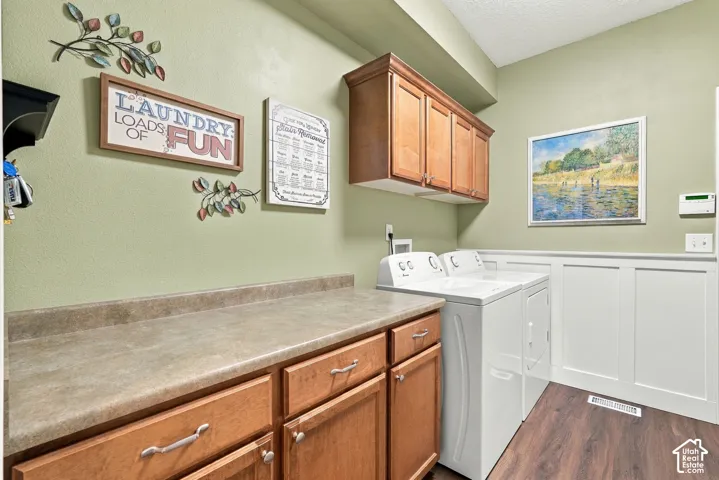 Laundry room featuring wood-finish flooring, shaker-style cabinetry, a solid-surface countertop, and white wainscoting