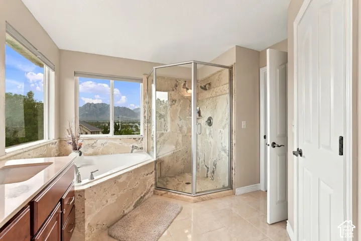 Corner soaking tub and separate glass-enclosed shower featuring stone tile surround, stone-topped vanity, and mountain scenery
