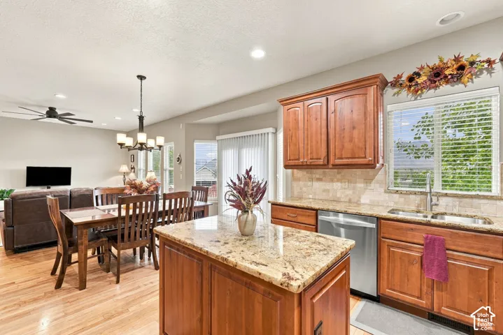 Kitchen featuring natural wood cabinetry, stone-surface countertops, central island, tiled backsplash, and stainless steel dishwasher