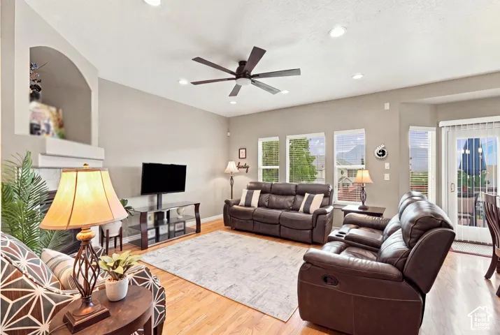 Living area featuring wood-finish flooring, recessed lighting, a ceiling fan, a fireplace with an arched alcove, and multiple windows
