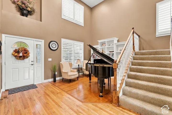 High-ceiling entryway featuring hardwood flooring, built-in shelving, white plantation shutters, and a staircase with a wooden banister