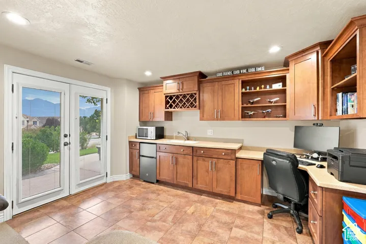 Built-in cabinetry with integrated wine rack, neutral solid-surface countertops, inset sink, tile flooring, and double glass-pane doors