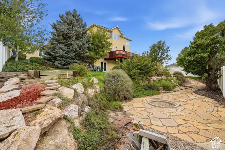 Multi-level backyard featuring natural stone landscaping, tiered retaining walls, a stone-paved patio with a built-in fire pit, and an elevated wood deck