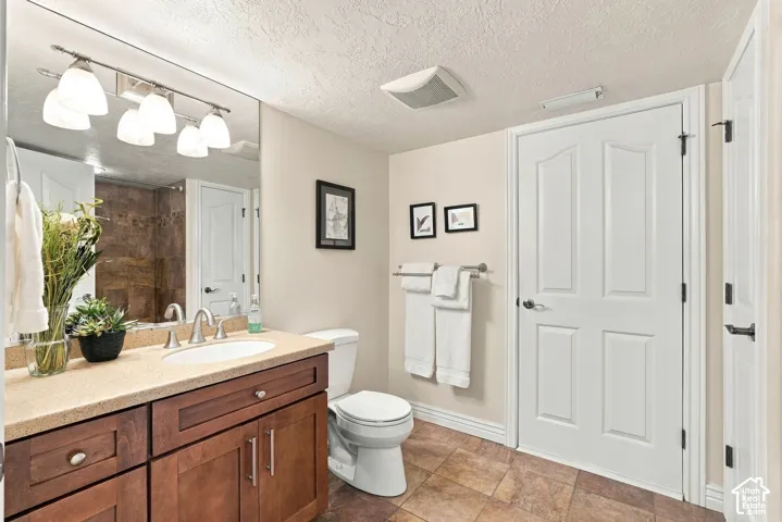 Bathroom featuring a dark wood-finish vanity with a stone countertop, an integrated oval sink, multi-bulb vanity lighting, and tile flooring