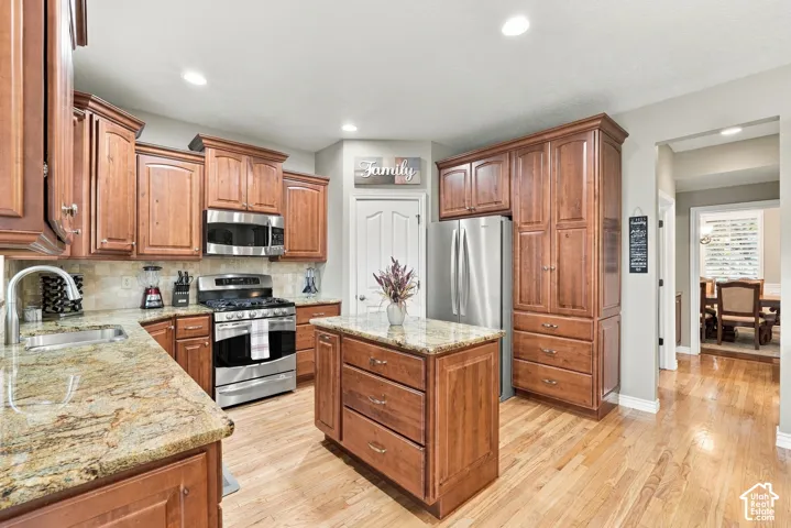 Kitchen featuring shaker-style cabinetry, stone countertops, a central island with storage, stainless steel appliances, and wood-finish flooring