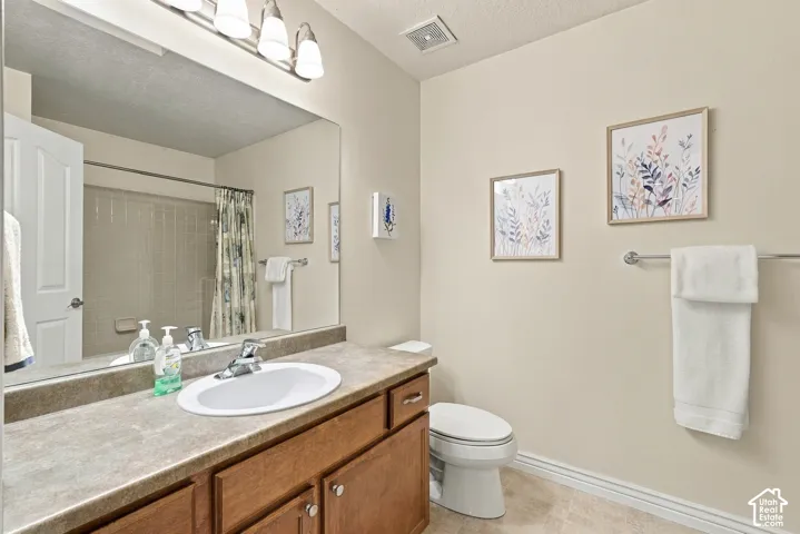 Bathroom featuring a wood-finish vanity, solid-surface countertop, oval undermount sink, wall-spanning mirror, and a four-bulb light fixture